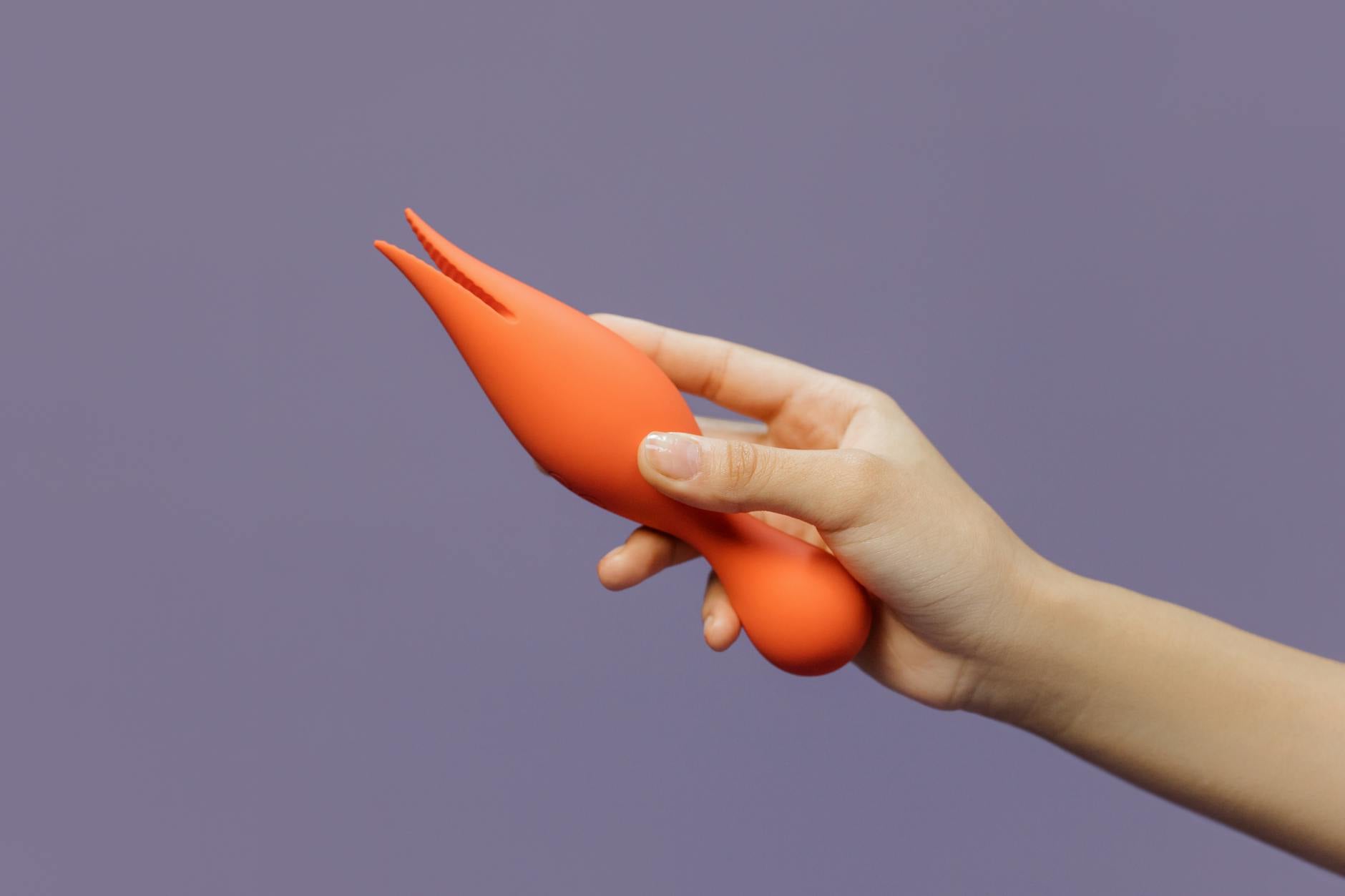 A hand holding a lemon-colored vibrator against a minimalistic purple backdrop, showcasing modern sensuality and self-care