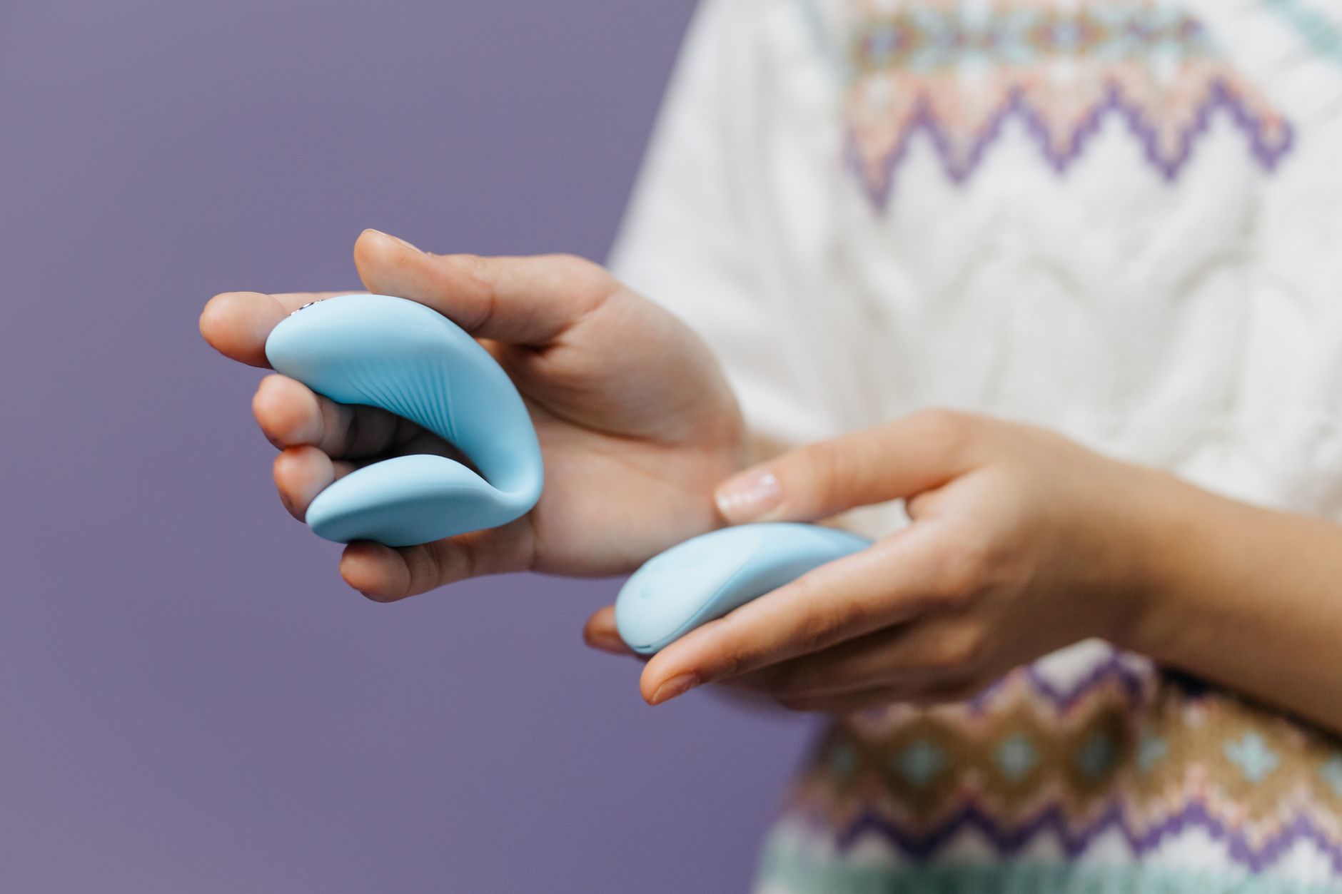Close-up of hands holding a sleek vibrator against a purple background, representing intimate self-care and clitoral pleasure.