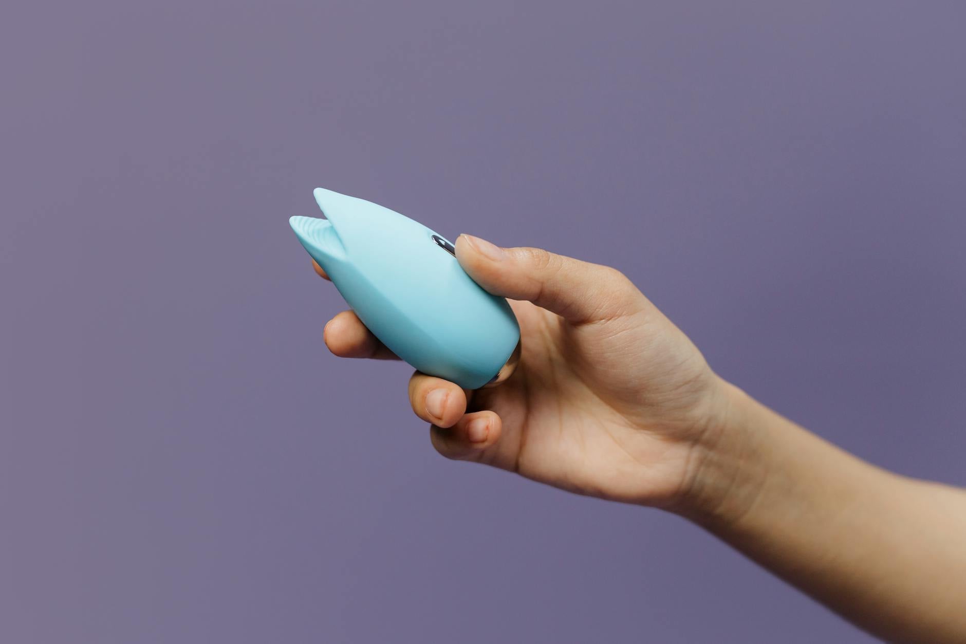 A blue silicone vibrator held in hand against a purple background, representing comfort with sexuality and self-exploration